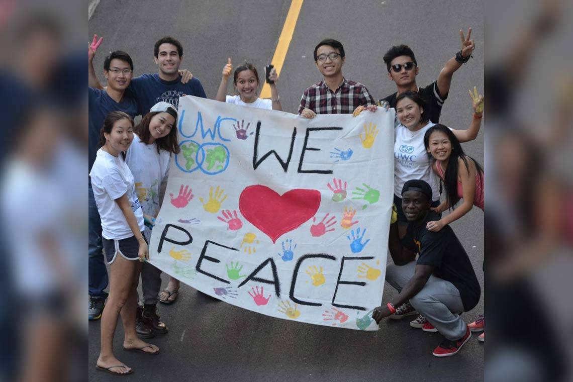 10 students from UWC schools pose with a hand-painted banner that reads 'UWC WE <3 PEACE'
