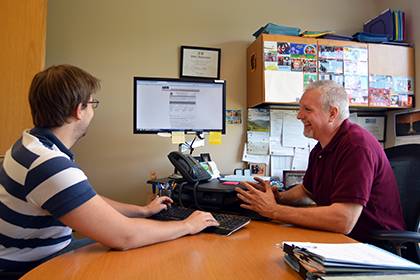 Anthony Keller, right, explains an online hiring form to Ph.D. student Paul Sommerfeld. Keller uses the summer as a time to finalize student hires from the spring and prepare for another influx in the fall. Photo by Bryan Roth.