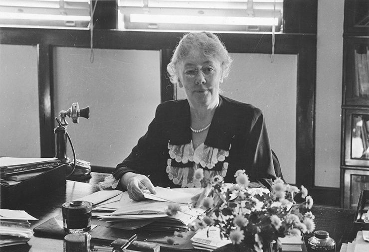 A woman sits behind a desk with an old-fashioned phone to her left