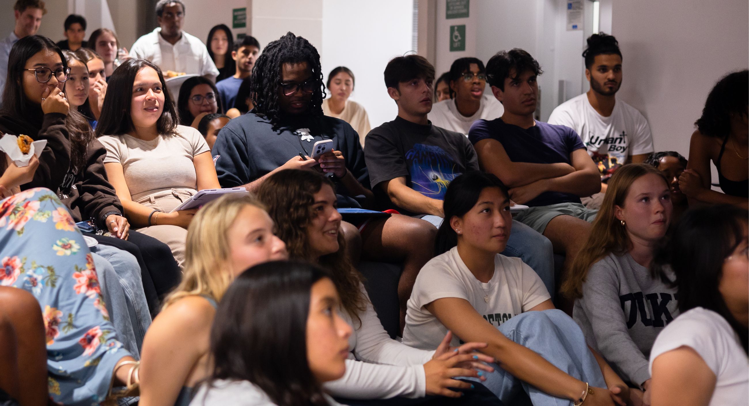 Students in a dorm, some looking shocked, watch a program on TV.