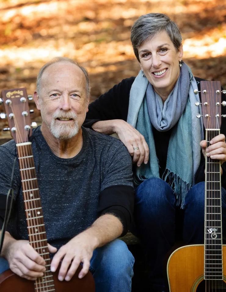 A man and a woman sit while holding acoustic guitars