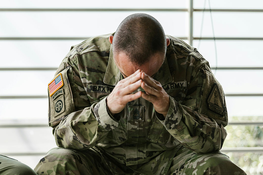 A man in a military uniform with his head resting on his hands