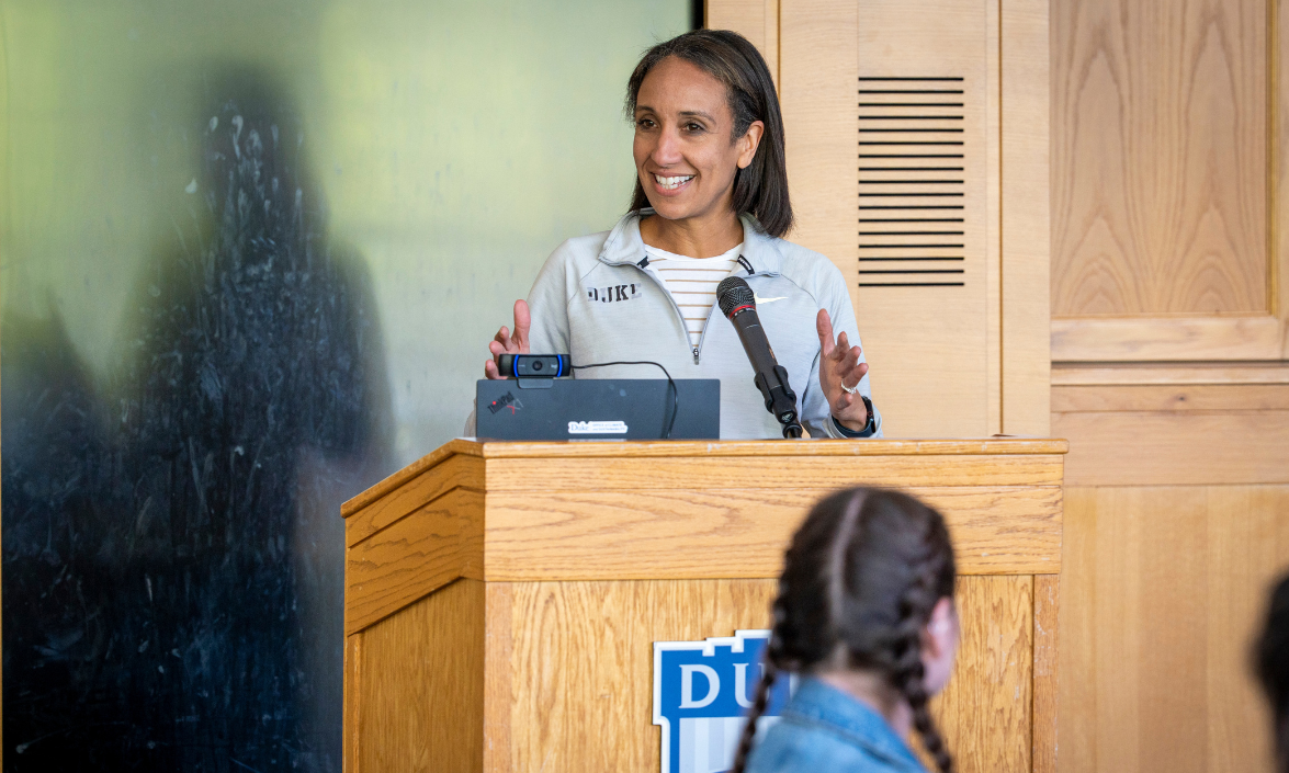 A woman standing at podium is speaking to an audience.