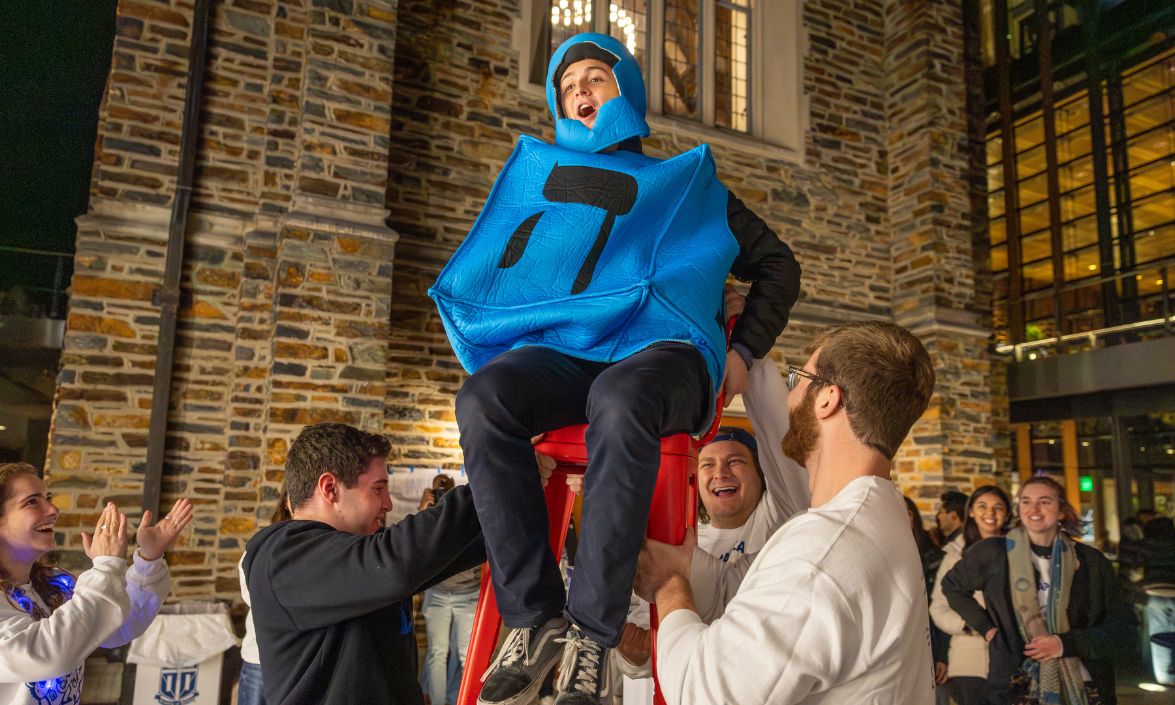 A student dressed up as a dreidel being lifted onto a chair.