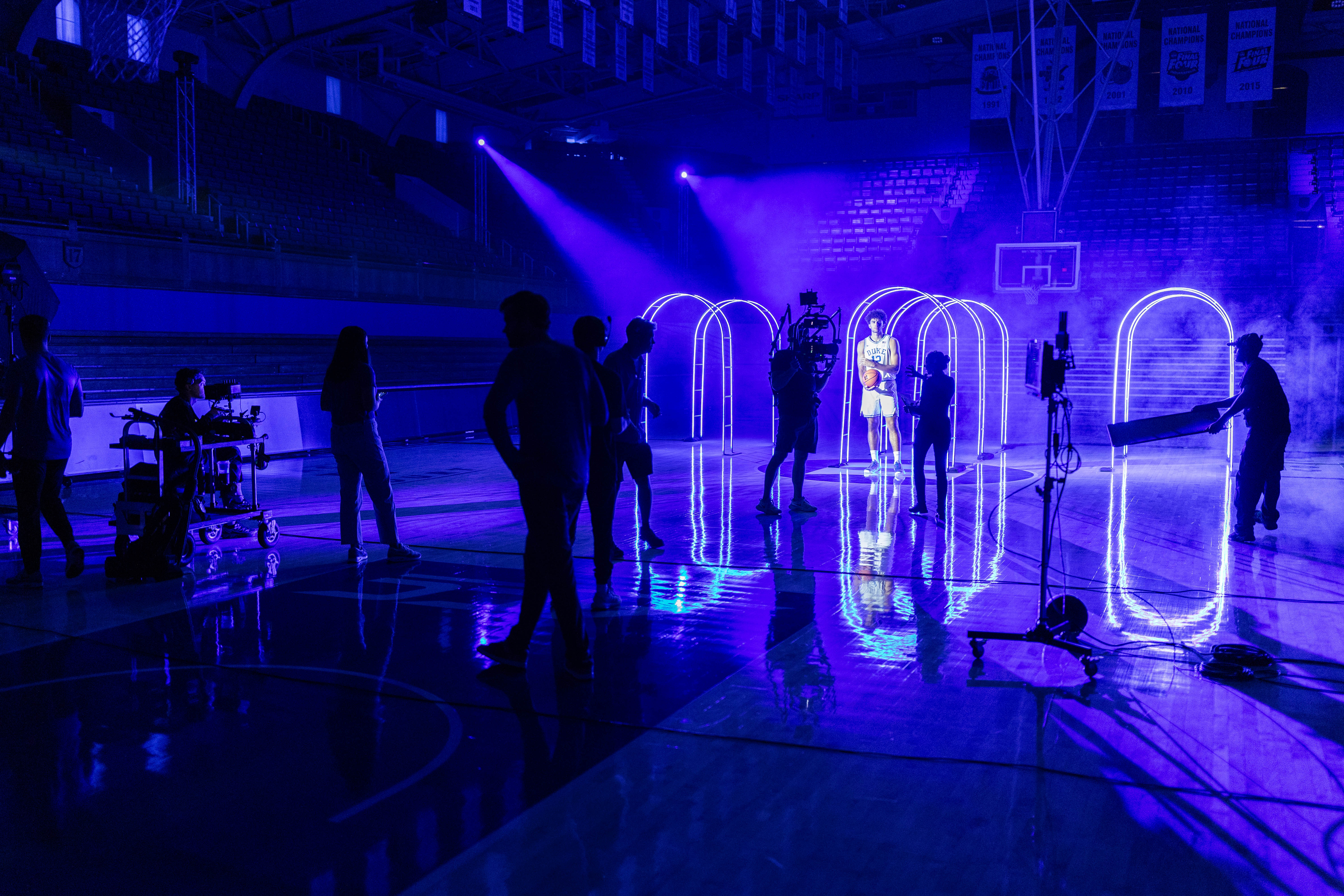 a Duke men's basketball player stands in front of three neon arches for a photo shoot