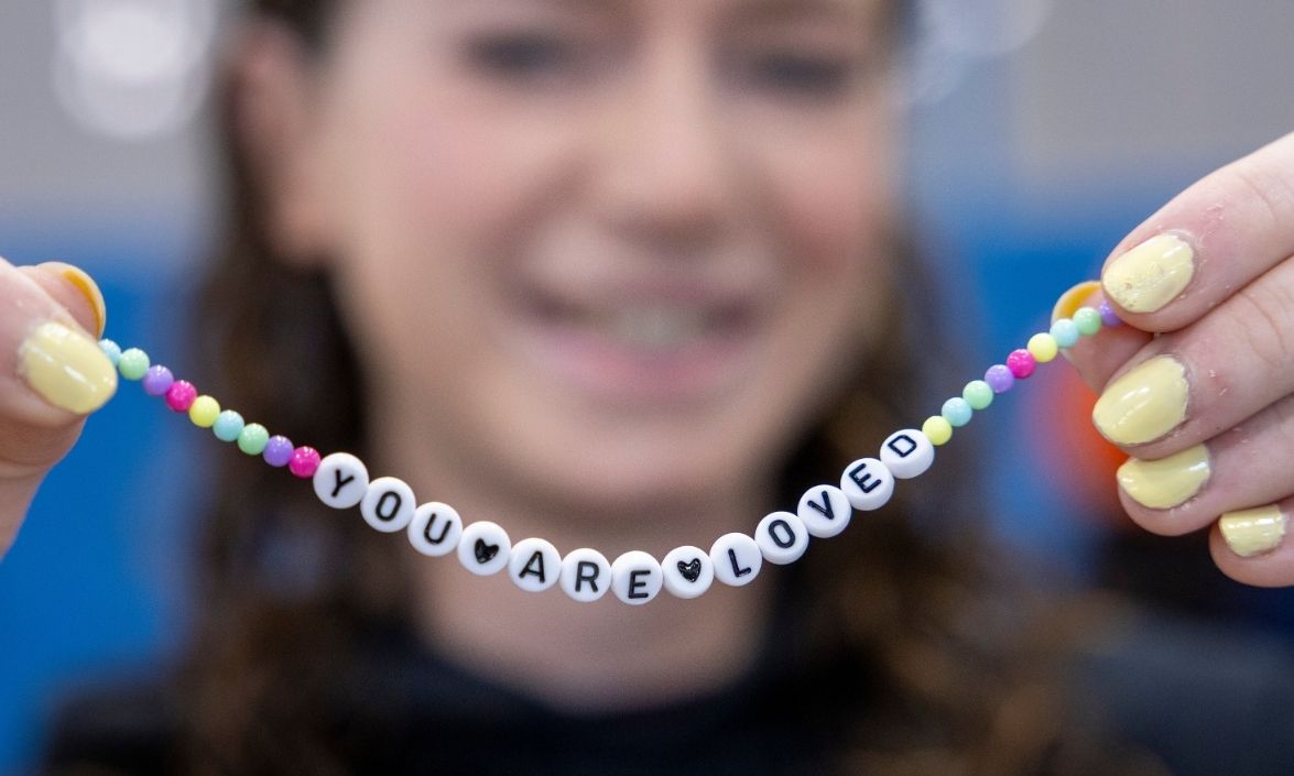A person holding up a bracelet that says 'you are loved'