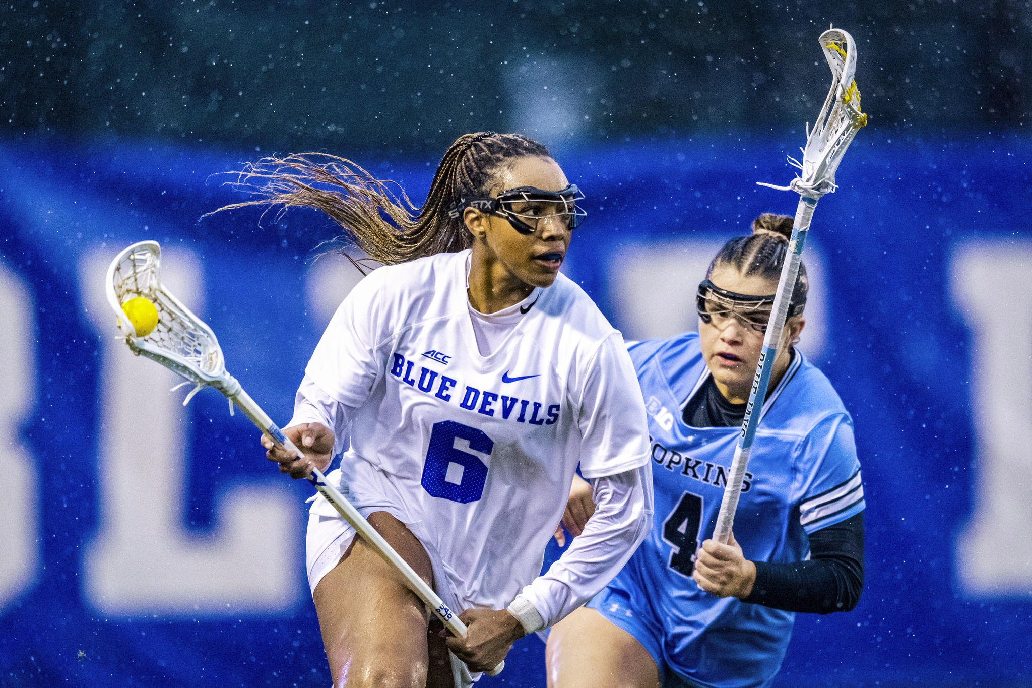 Two women in a lacrosse match in the rain