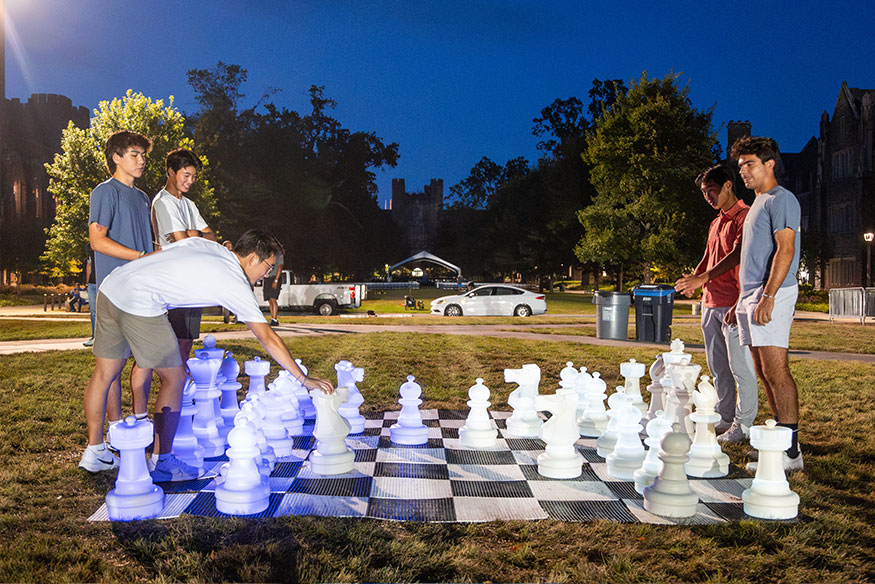 A group plays lawn chess on the quad