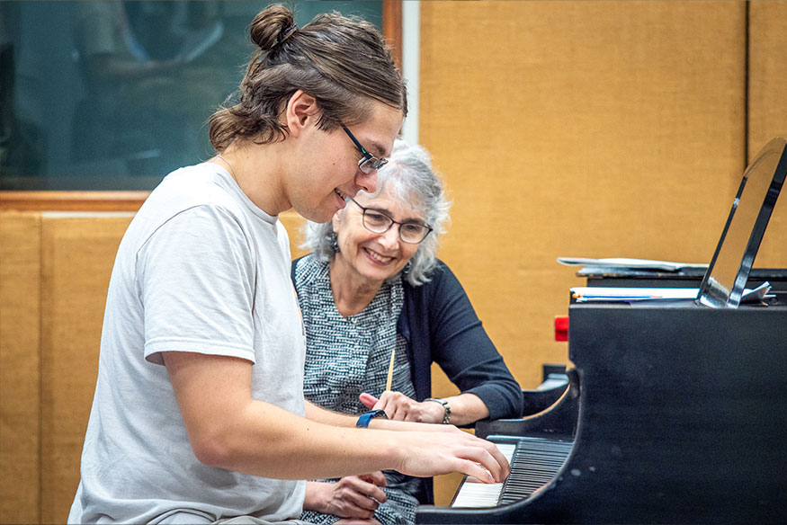A student at the piano with the instructor looking on
