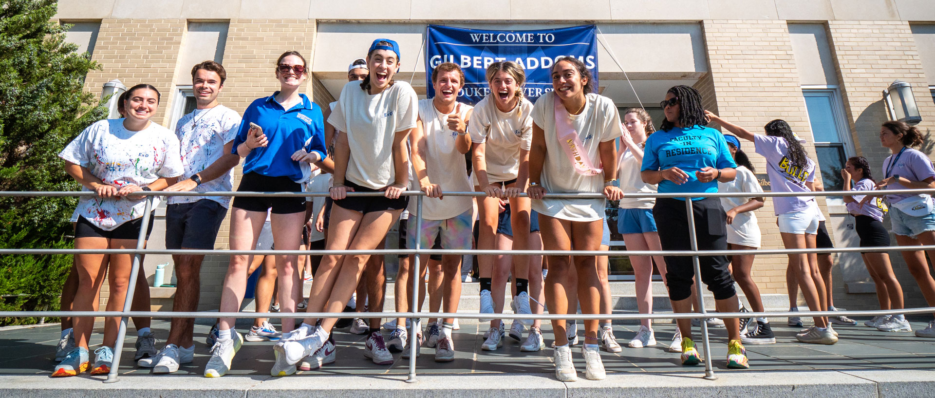 Orientation leaders smiling and hanging over a railing, ready to get started moving student into the dorm