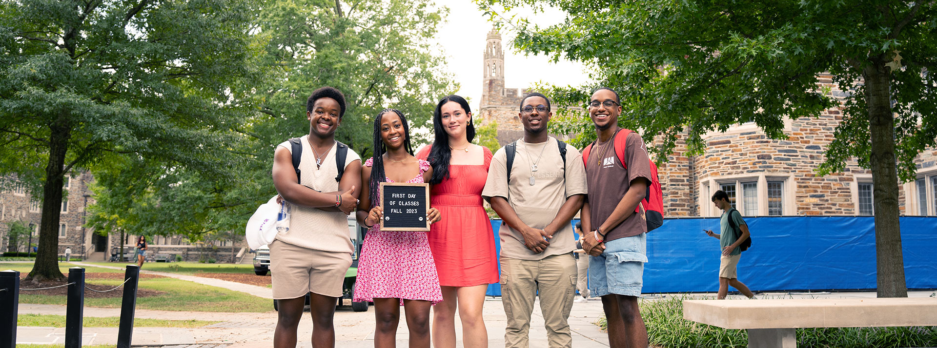Five students standing on a west campus path with Duke architecture in the background holding a sign that says, “First day of class Fall 2023”