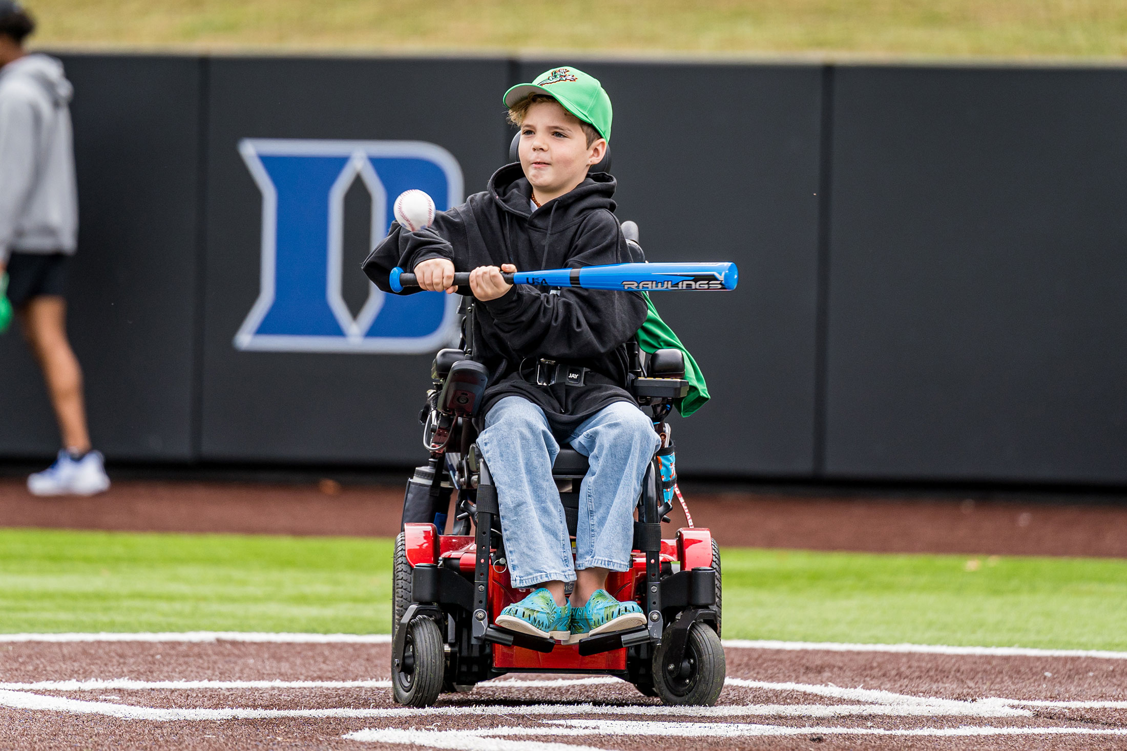 child in wheelchair swings at a pitch in Coombs Stadium.