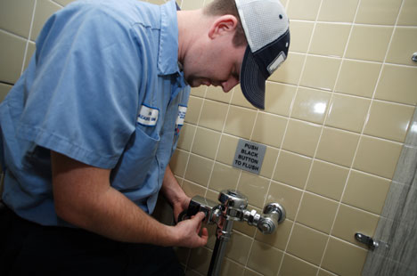 Kevin Brinn, 27, a general maintenance mechanic with Duke's Facilities Management Department, uses electrical tape to cover a sensor on an automatic flush toilet in Duke Divinity School. Auto flush toilets, where possible on campus, are being switched to manual to conserve water. 