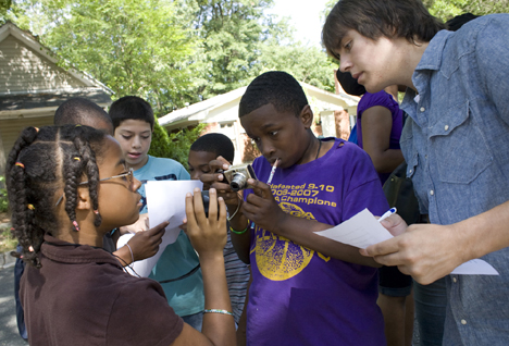 Duke student Casey Dunn, right, watches as Deja Cooper, 13, left, and Kendall Clark, 13, center, use a GPS unit and camera to recording the coordinates of a house while on a walking tour through Walltown. 