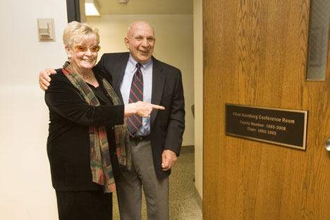 Allan Kornberg and his wife, Pat, pose by a plaque on the door of the room named for the longtime political science faculty member. 