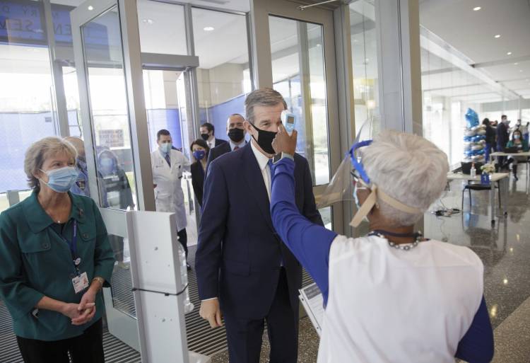 Gov. Cooper is greeted by Faye Williams who takes his temperature at the door to the hospital
