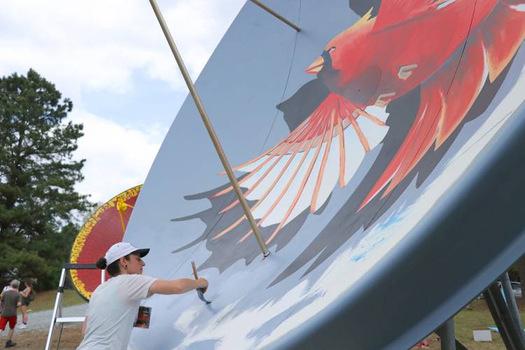 Artist works on a mural of a cardinal.