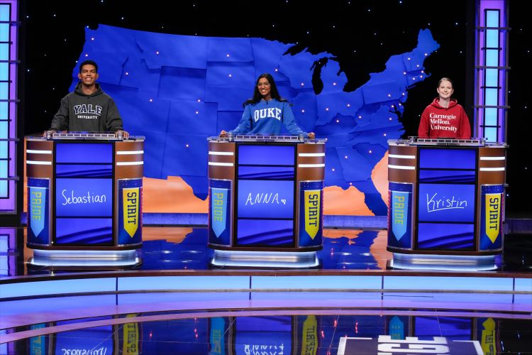 Three college students behind podiums on the "Jeopardy!" set. Duke student Anna Muthalaly is behind the center podium.