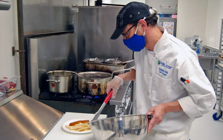 Chef Eduardo Polit plates chicken schnitzel and french fries onto a plate in the Freeman Center Café. Photo by Jack Frederick.