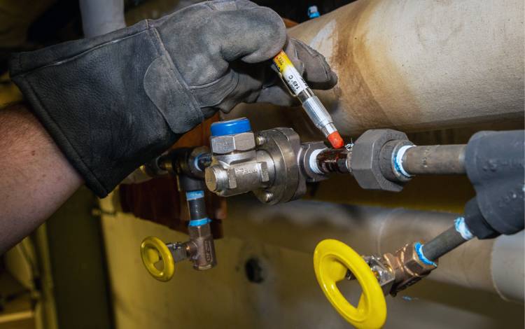 Yancey Leonard uses an orange crayon to measure the temperature of a steam trap.