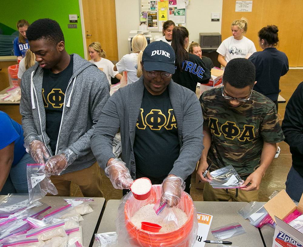 unde Abu, Serges Himbaza, and Lee Barnes, senior members of the Alpha Phi Alpha fraternity, along with other Duke community members commemorate the MLK holiday during a meal-packing event at Durham Tech. Photos by Megan Mendenhall/Duke Photography