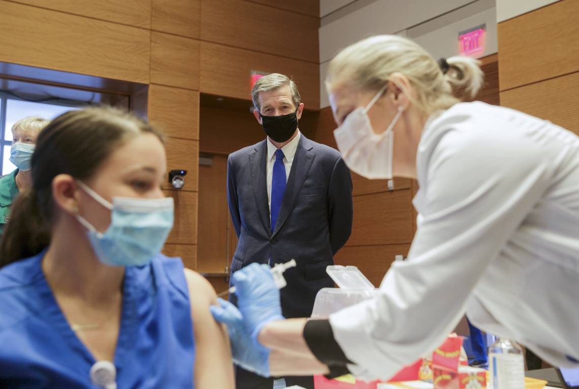 Governor Roy Cooper watches as a Duke Health employee receives their vaccination