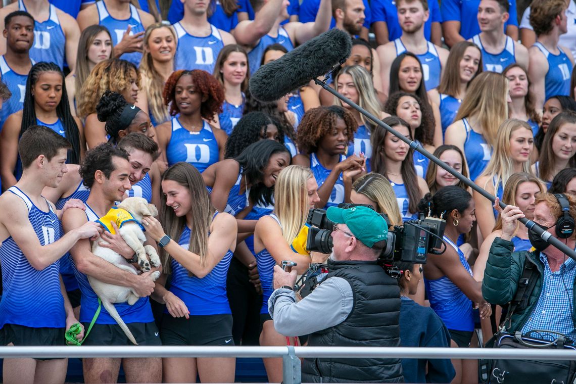 A 60 Minutes film crew captures members of the Duke track team embracing a kindergarten puppy. Photo by Jared Lazarus