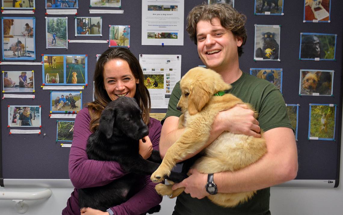 Vanessa Woods, left, holds Ernie while Brian Hare carries Kyler. The two puppies are being trained to become assistance dogs.