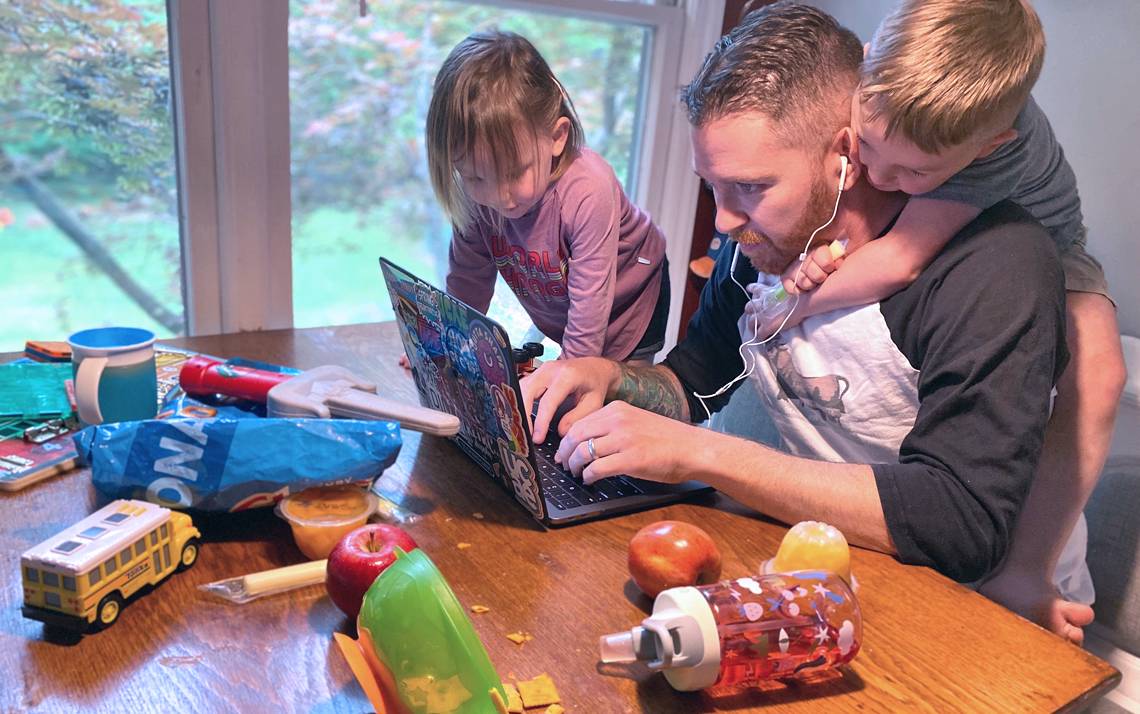 Kyle Fox working at his laptop with his children.