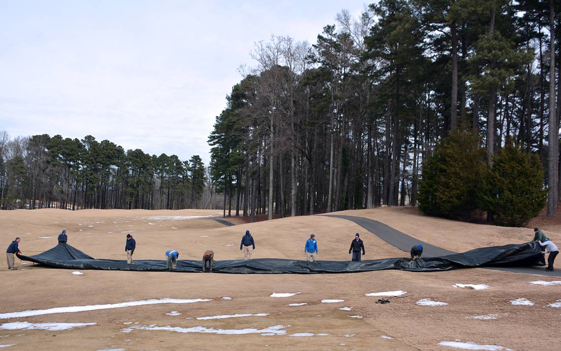 Members of the Duke University Golf Club Maintenance Team roll up a tarp after snowy weather.