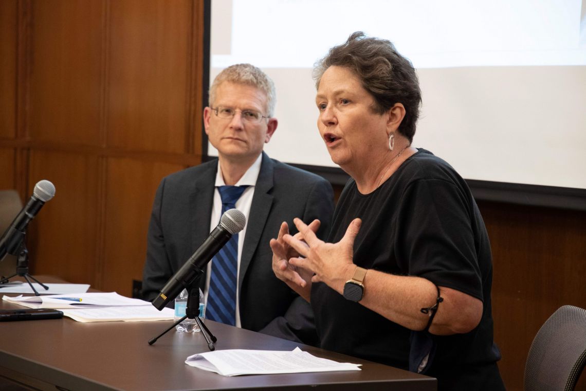 Professor Robin Kirk is seated at a table with professor Neil Siegel. Kirk is speaking and gesturing with her hands.