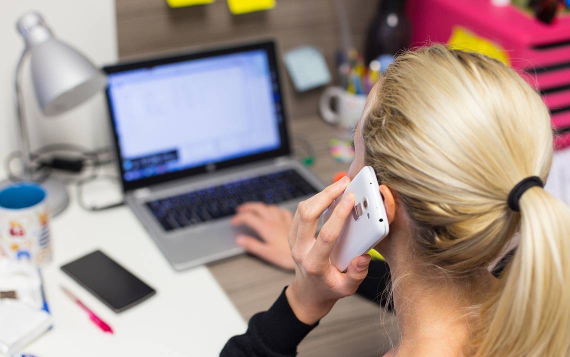 A woman talks on her phone while also using her computer.