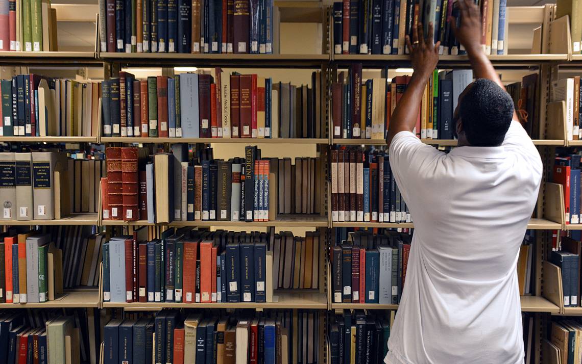 Joseph Bailey, library assistant for stacks maintenance and retrieval, places a copy of “A History of Medicine in 50 Objects” on a shelf in Bostock Library.