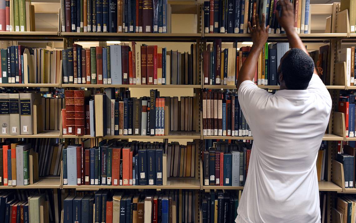 Joseph Bailey, library assistant for stacks maintenance and retrieval, places a copy of “A History of Medicine in 50 Objects” on a shelf in Bostock Library. 