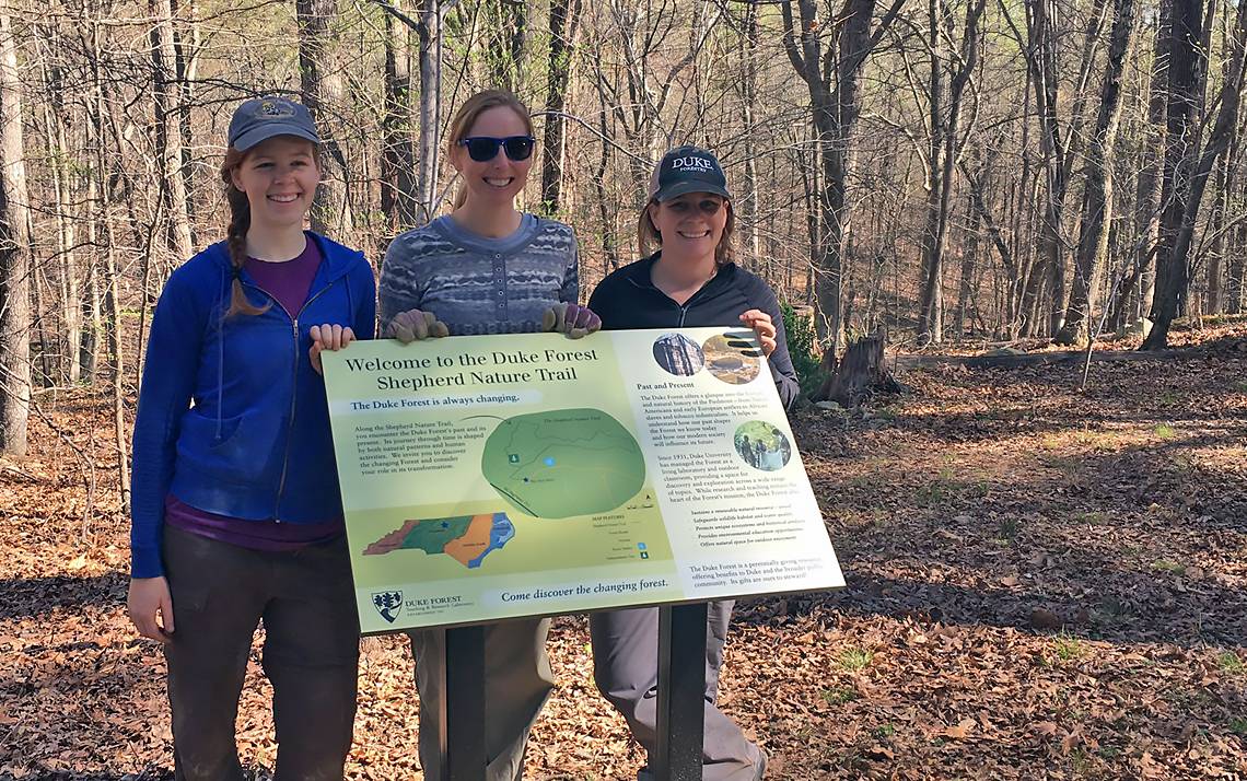 From left to right: Maggie Heraty, left, Shepherd Nature Trail project intern, Duke Forest Director Sara Childs, center, and Duke Forest Operations Manager Jenna Schreiber, right, in front of a new interpretive sign.