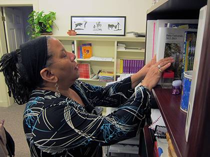 Pat McPherson arranges items on a bookshelf in her office. It features personal items as well as books and information for the variety of responsibilities she holds.