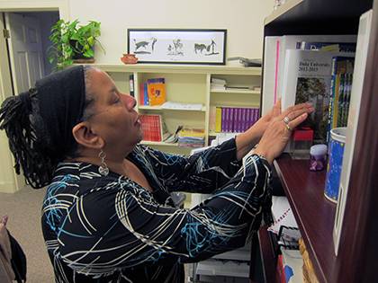 Pat McPherson arranges items on a bookshelf in her office. It features personal items as well as books and information for the variety of responsibilities she holds. 