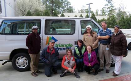 Laura Alvis, sitting and in the orange sweater, poses with her vanpool group before leaving for work in Durham. The group vanpools from Mebane to Duke each day. Photo courtesy of Laura Alvis.