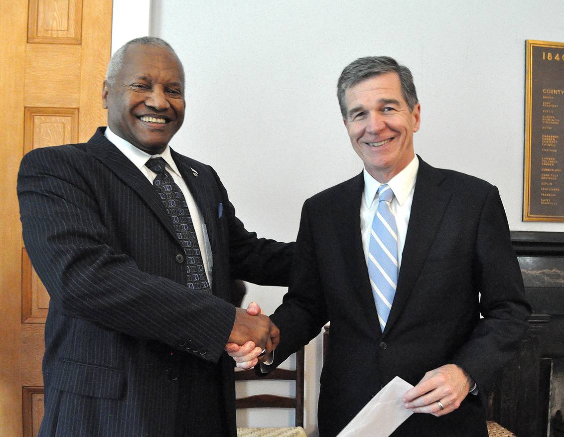 Phail Wynn presents Gov. Roy Cooper with the Doing Good check. Photo by April Dudash.