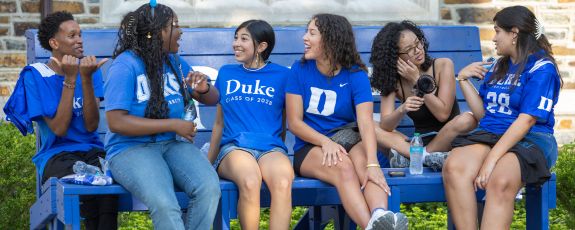 Students talk while sitting on a bench on the quad