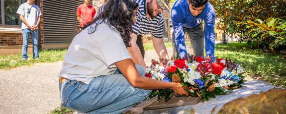 ﻿Juniors Ranjan Jindal, VP of Keohane Quad, Tara Singh, President of Keohane Quad, and Austin Brown, Communications Coordinator for Keohane Quad lay a wreath at Duke’s 9/11 Memorial plaque near the grove of six trees planted behind Keohane Quad