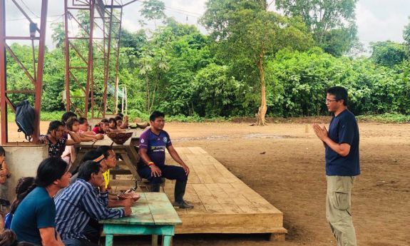 Duke researcher William Pan, standing, wearing a blue shirt, speaks with seated Peruvians in an outdoor setting.