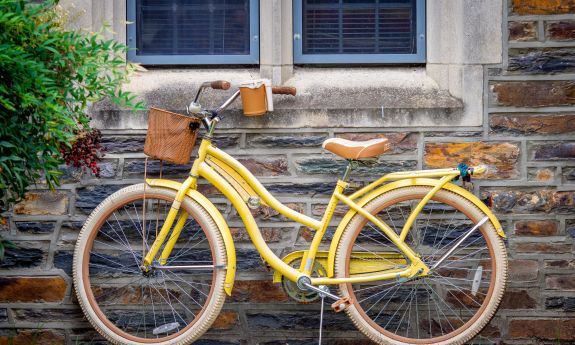 A yellow bike rests against a brick wall