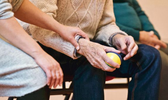 A young person sits and holds the hand of an older person