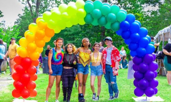 Group of students standing under a rainbow of balloons. 