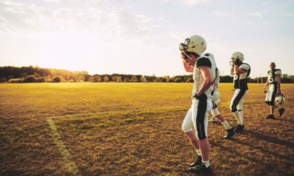 high school football students walk off field after a hot practice