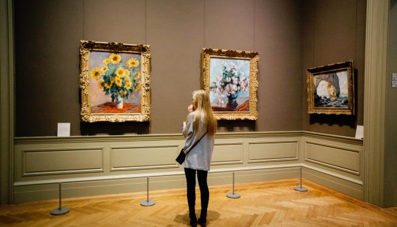 A woman stood looking at a painting of flowers at an art museum