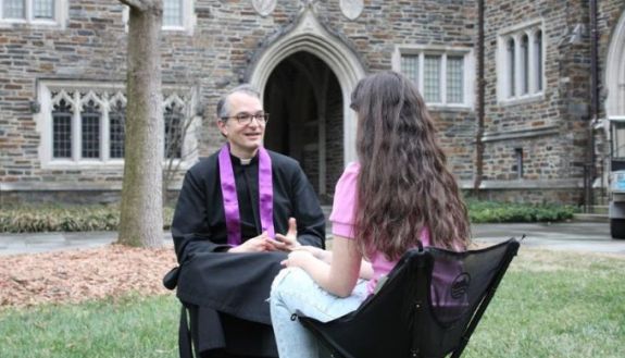 Father Juan José Hernández sits with a student on the quad between the Kilgo and Craven buildings.