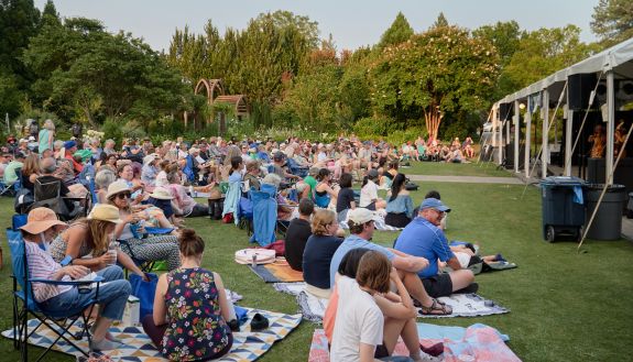 people sitting on a lawn for a concert in the gardens