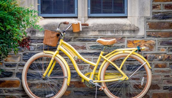 A yellow bike rests against a brick wall